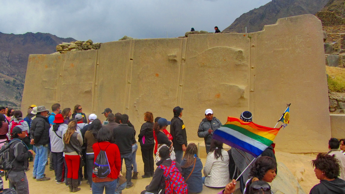 Wall in Ollantaytambo made by huge stones, the rainbow flag of the Quechua and a lot of tourists	